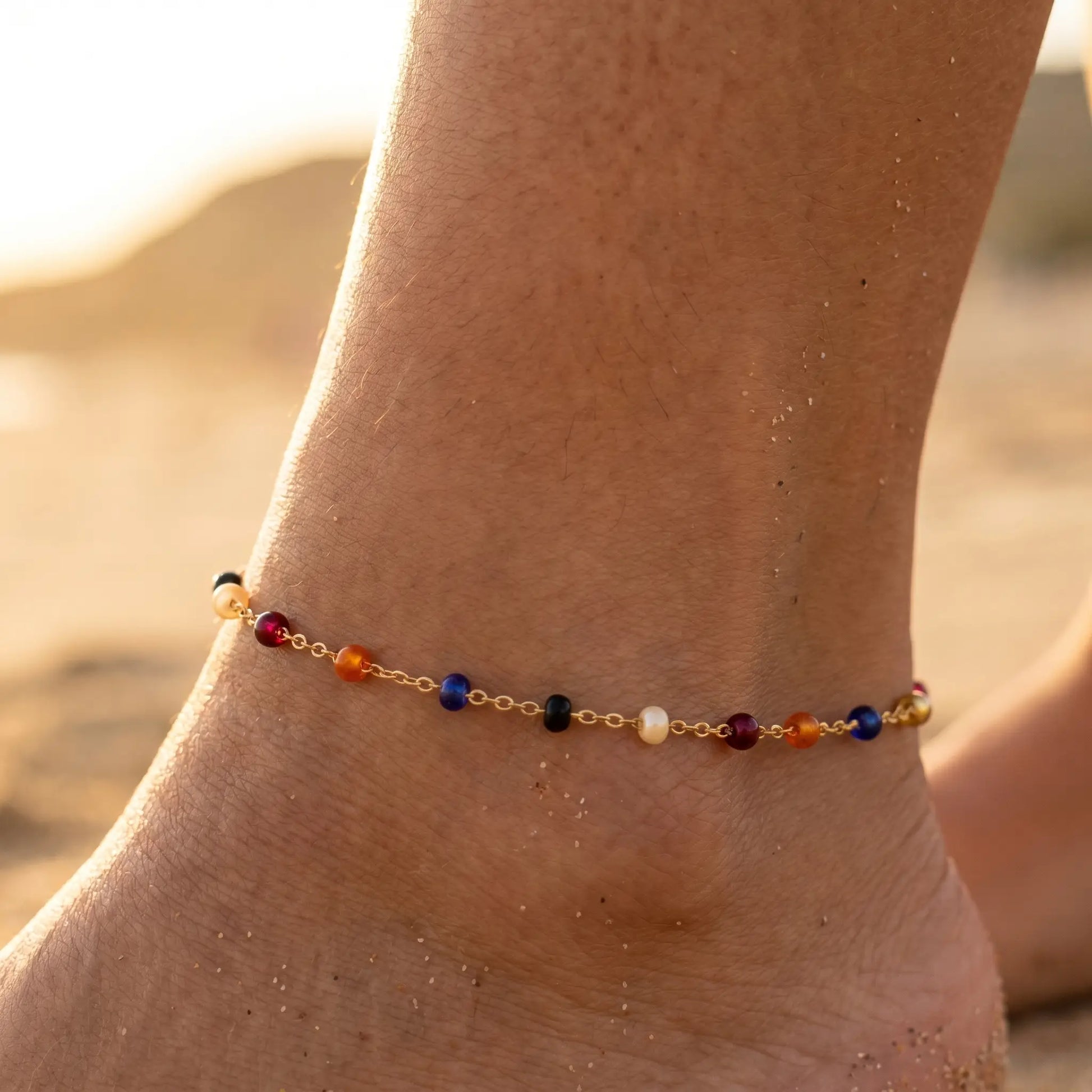 Multicolor bead anklet on tanned ankle at golden hour beach close-up