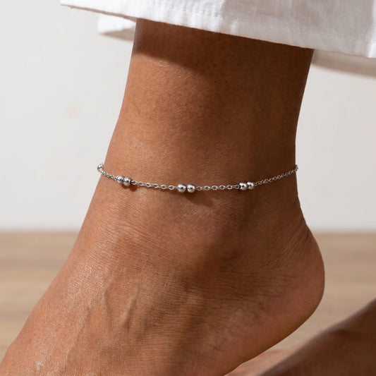 Silver beaded station anklet worn on dorsal ankle — woman's foot, dainty silver bead pair pattern in close-up