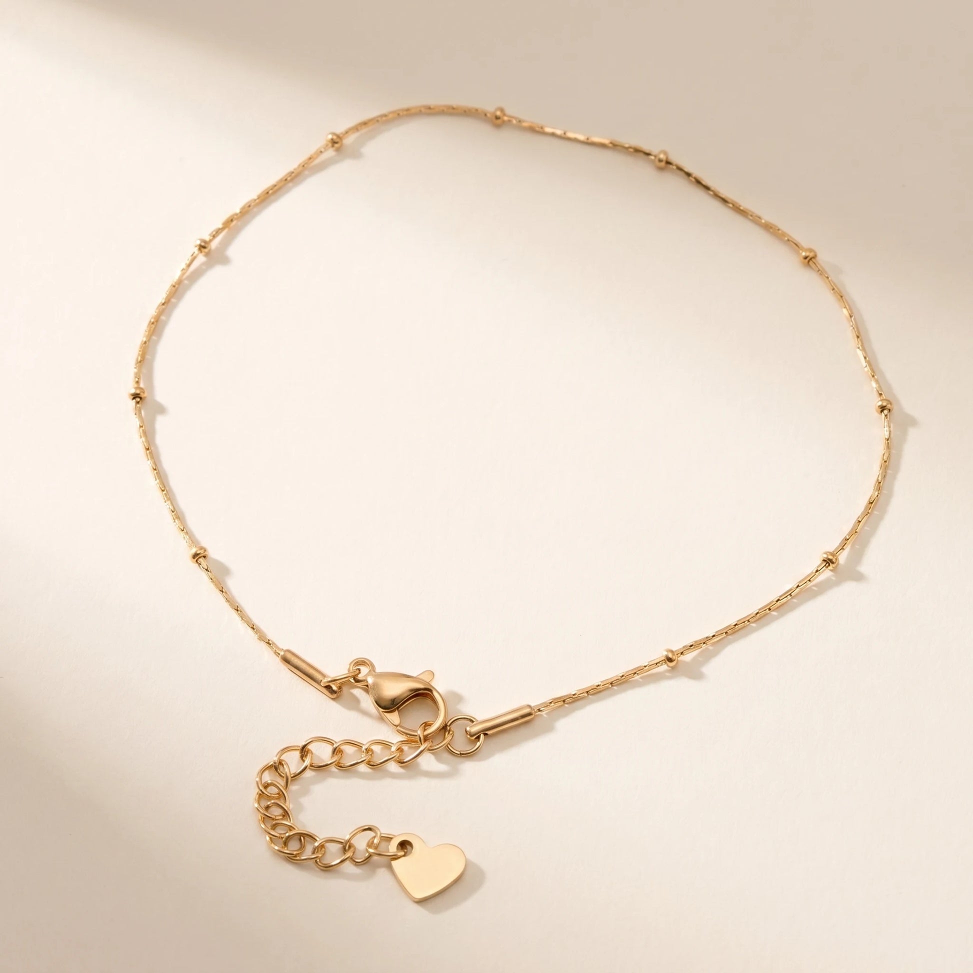 Gold satellite beaded chain anklet with tiny heart charm dainty packshot off-white background