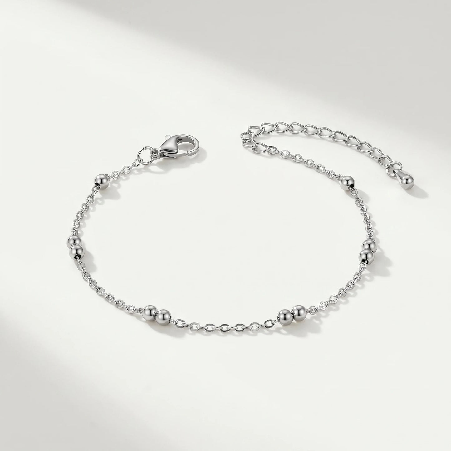 Silver beaded station anklet packshot on cool ivory background — dainty stainless steel cable chain with 4 silver bead pairs and teardrop charm