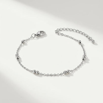 Silver beaded station anklet packshot on cool ivory background — dainty stainless steel cable chain with 4 silver bead pairs and teardrop charm
