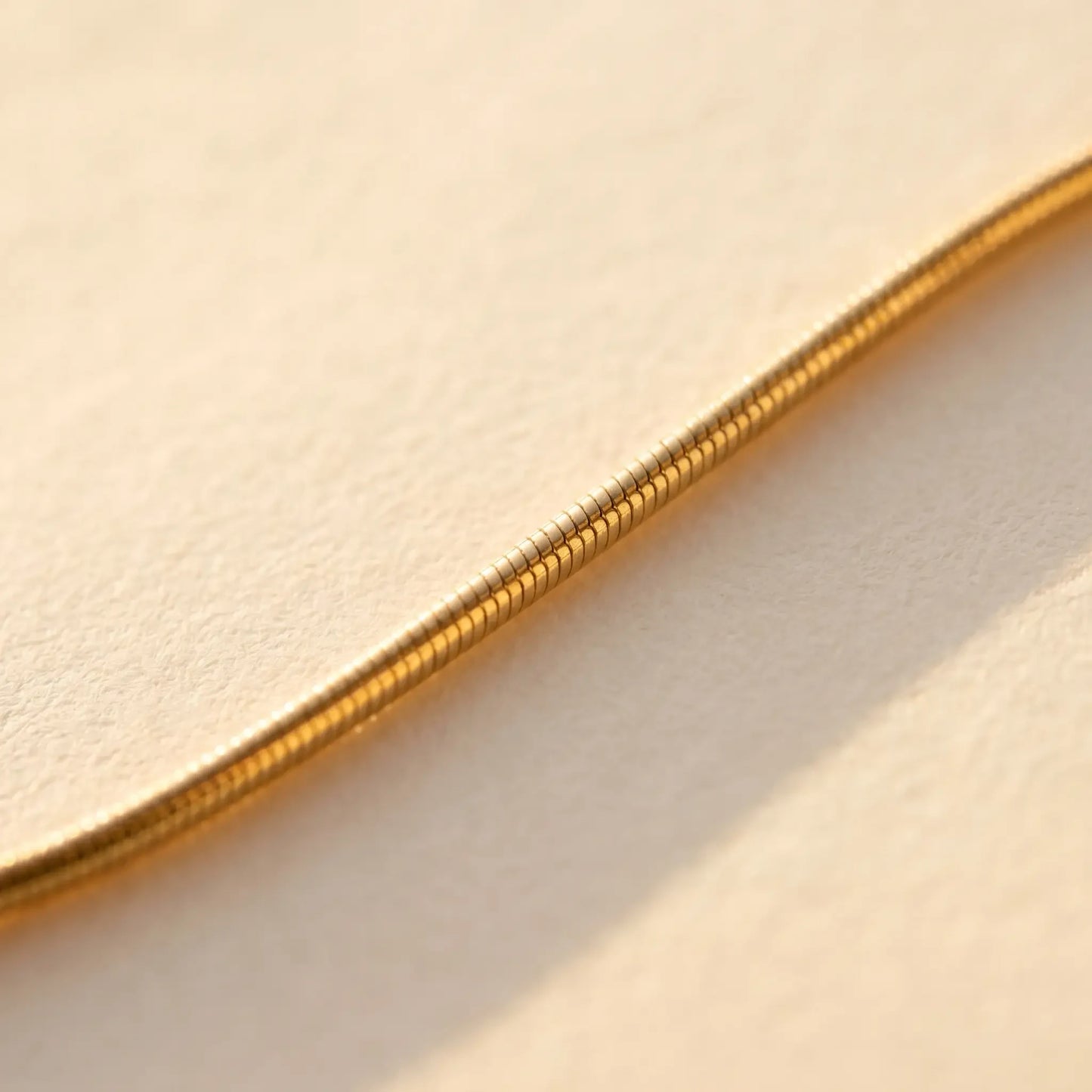 Gold snake chain macro detail showing smooth round tubular cross-section