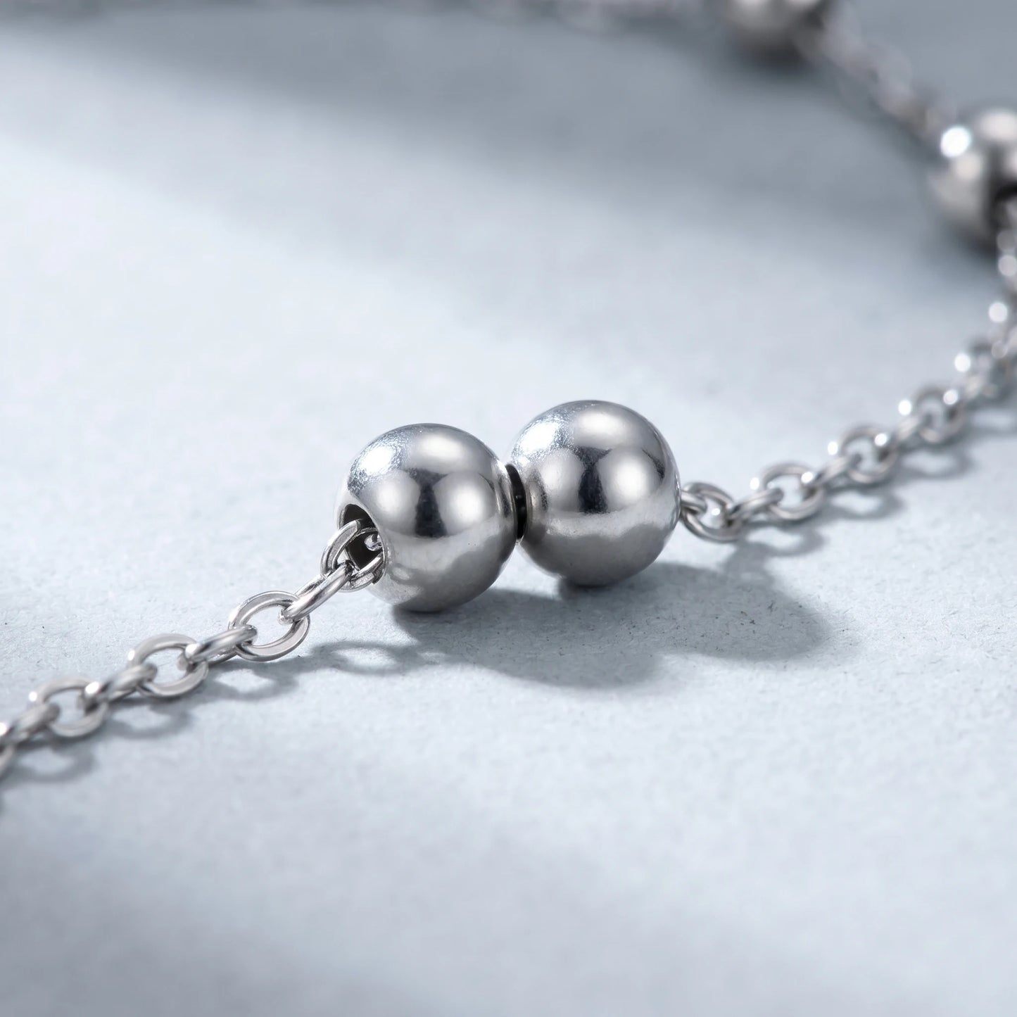 Macro detail of silver bead pair on dainty cable chain — stainless steel polished silver beads