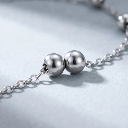 Macro detail of silver bead pair on dainty cable chain — stainless steel polished silver beads