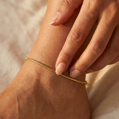 Intimate hand-to-anklet close-up showing dainty gold snake chain