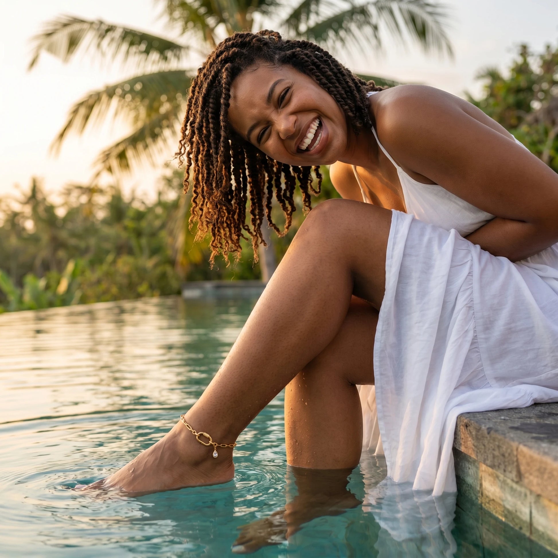 Joyful woman white maxi dress Bali infinity pool wearing gold carabiner paperclip anklet summer