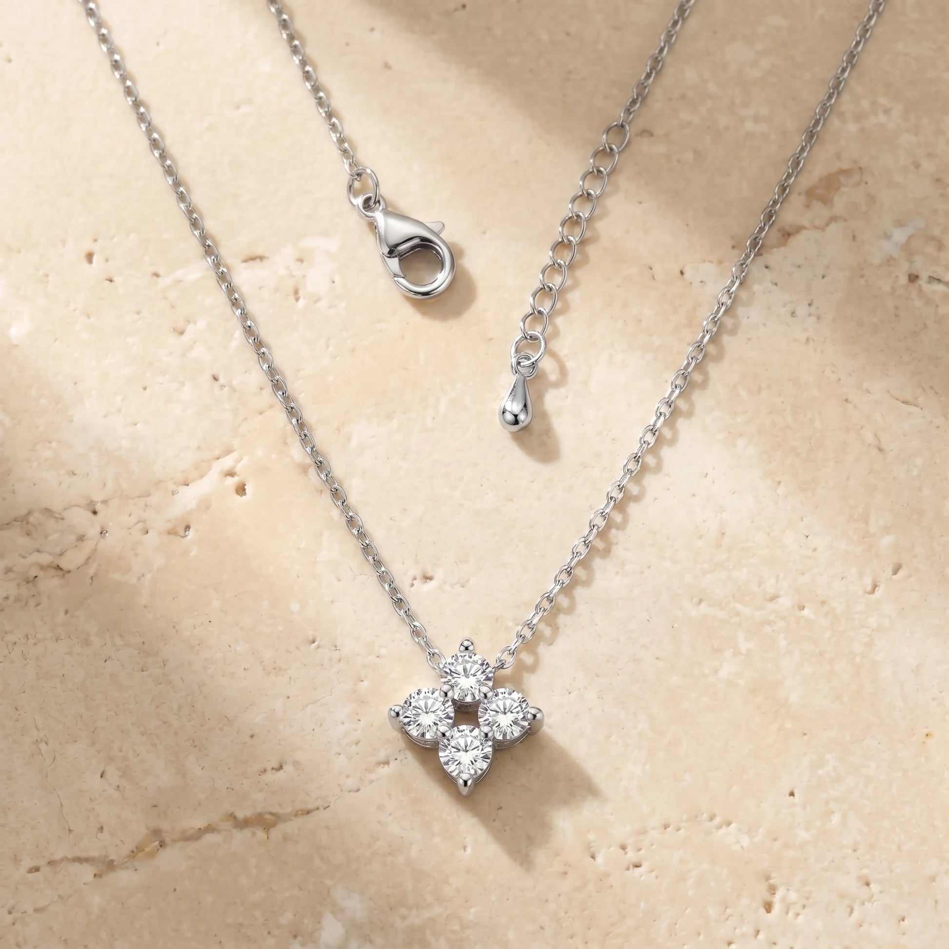 Diamond Cluster Necklace silver packshot — 4-stone CZ rhombus on warm travertine stone, dainty cable chain laid-flat, lobster clasp + teardrop extension visible