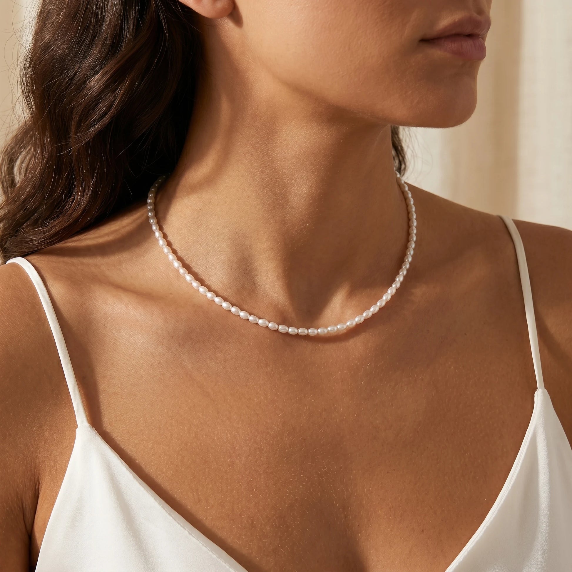 Tiny pearl strand necklace worn close-up at collarbone Italian woman white silk