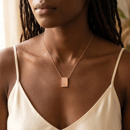 Rose gold rectangle pendant necklace worn close-up sharp 90 corners dark skin cream silk
