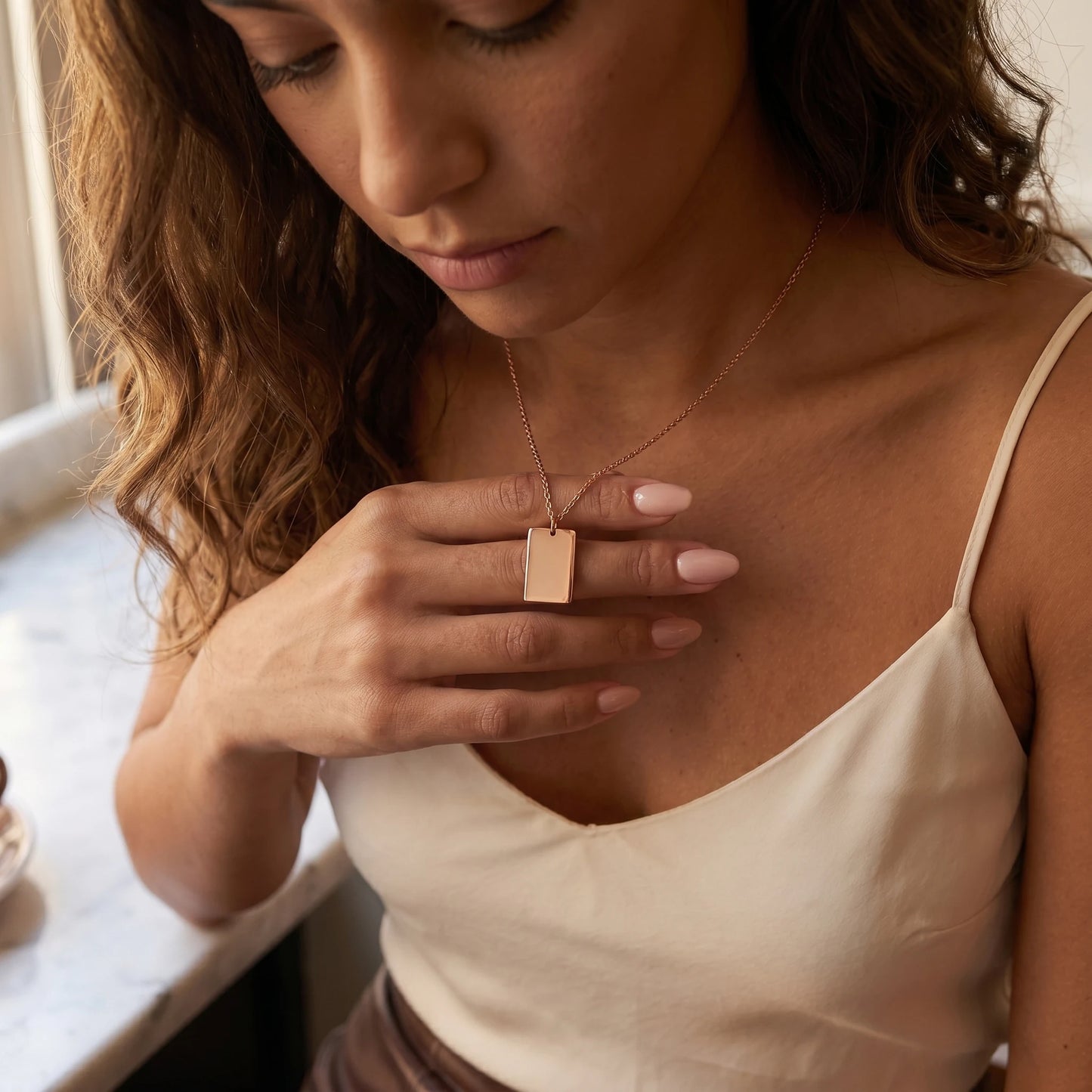 Rose gold rectangle pendant intimate hand-to-pendant moment Latina silk cami