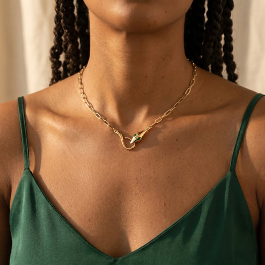 Gold snake pendant necklace worn close-up - entwined serpent clasp with emerald CZ eyes at collarbone