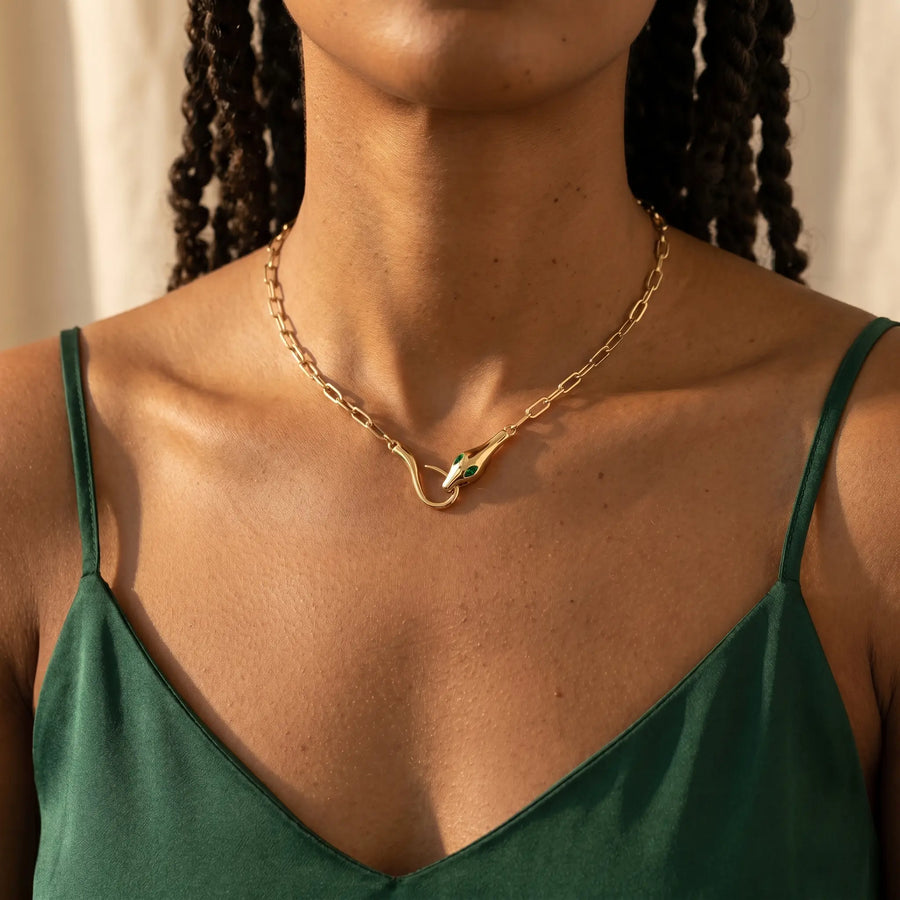 Gold snake pendant necklace worn close-up - entwined serpent clasp with emerald CZ eyes at collarbone