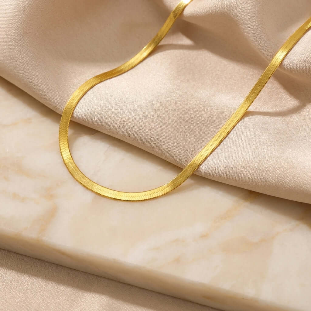 5mm Herringbone Chain showcased on elegant fabrics, highlighting AUREATE's liquid-gold aesthetics.