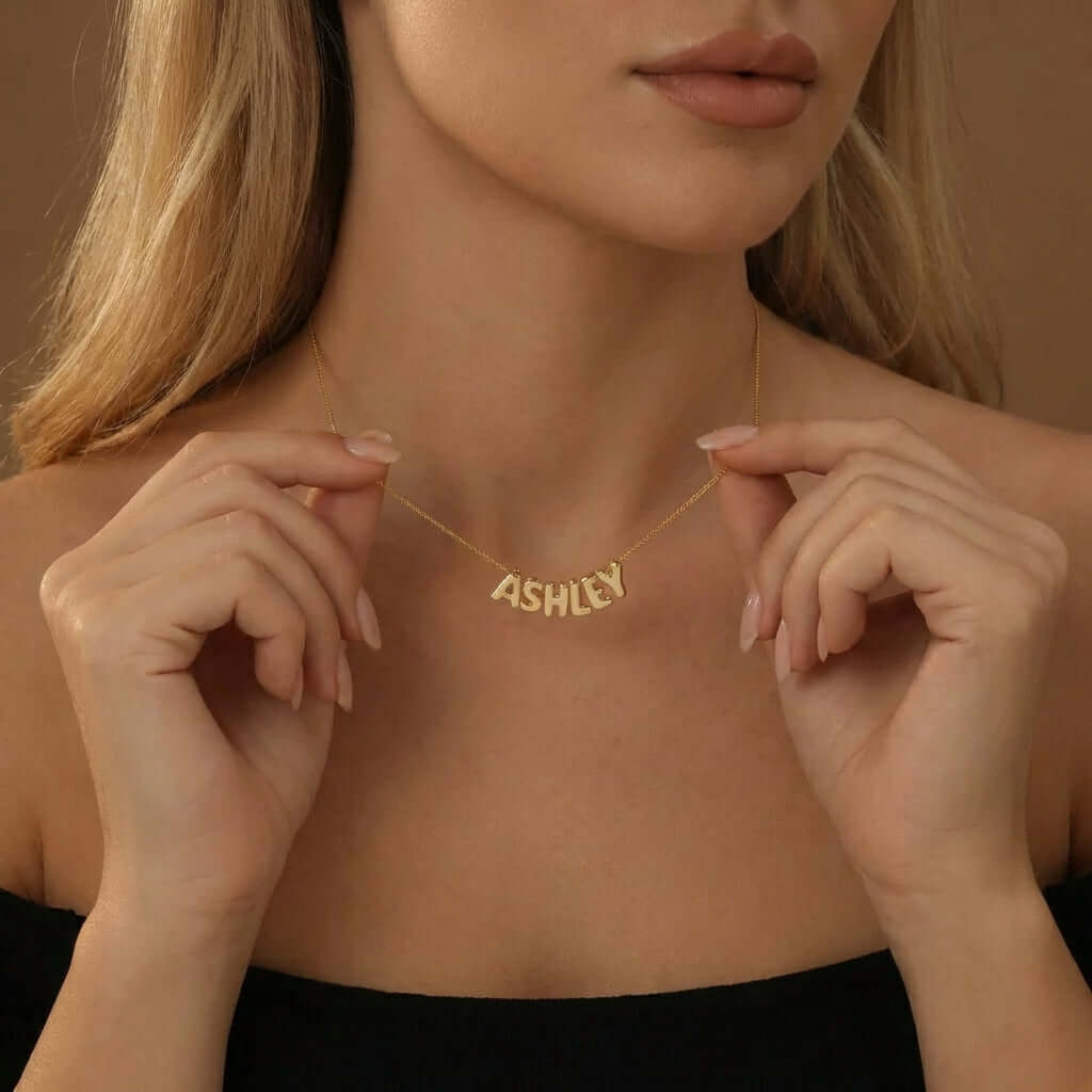 Woman wearing an AUREATE Bubble Style Name Necklace with the name ASHLY. Trendy puffy texture design for 2026.