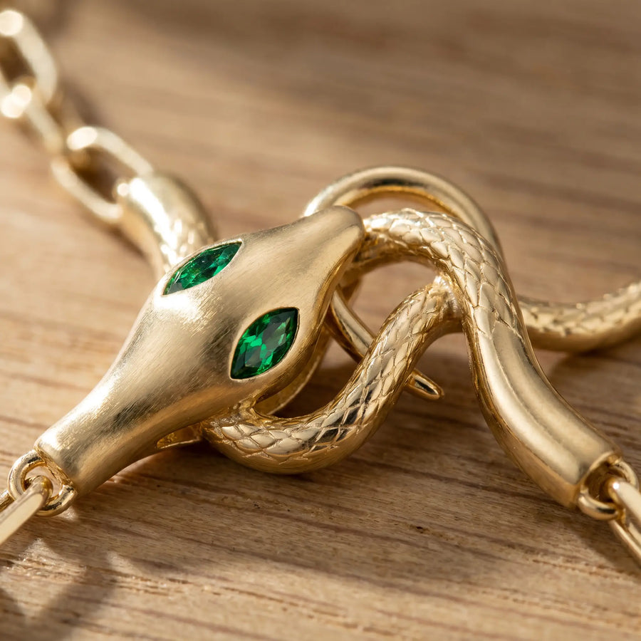 Snake pendant macro detail - 18K gold serpent heads with emerald green marquise CZ eyes and scale texture