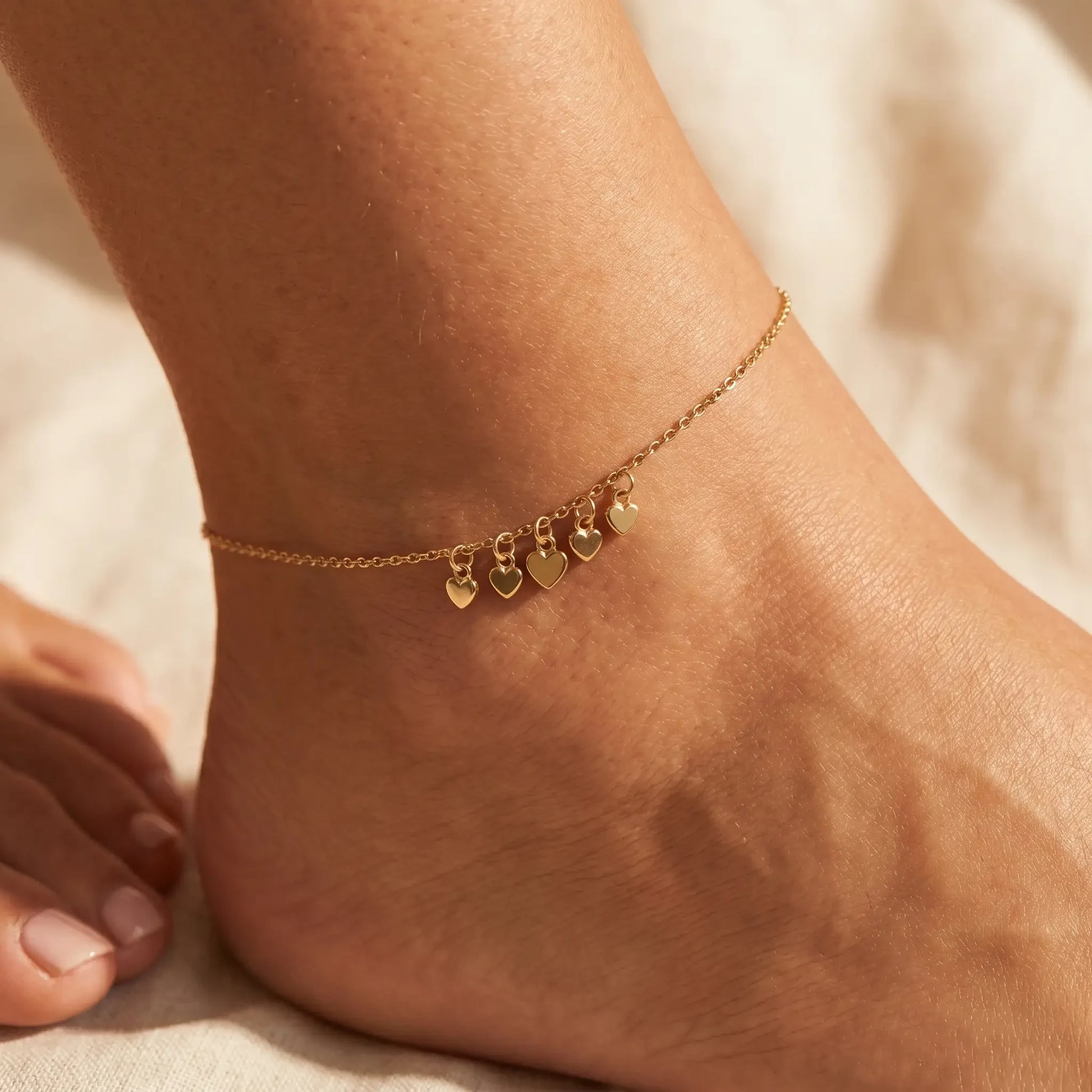 Tiny gold heart drop anklet worn close-up at ankle with sesame-seed-tiny heart cluster