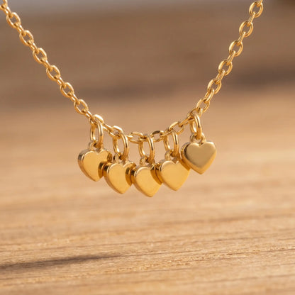 Macro detail of five tiny solid gold heart drop charms hanging from dainty cable chain