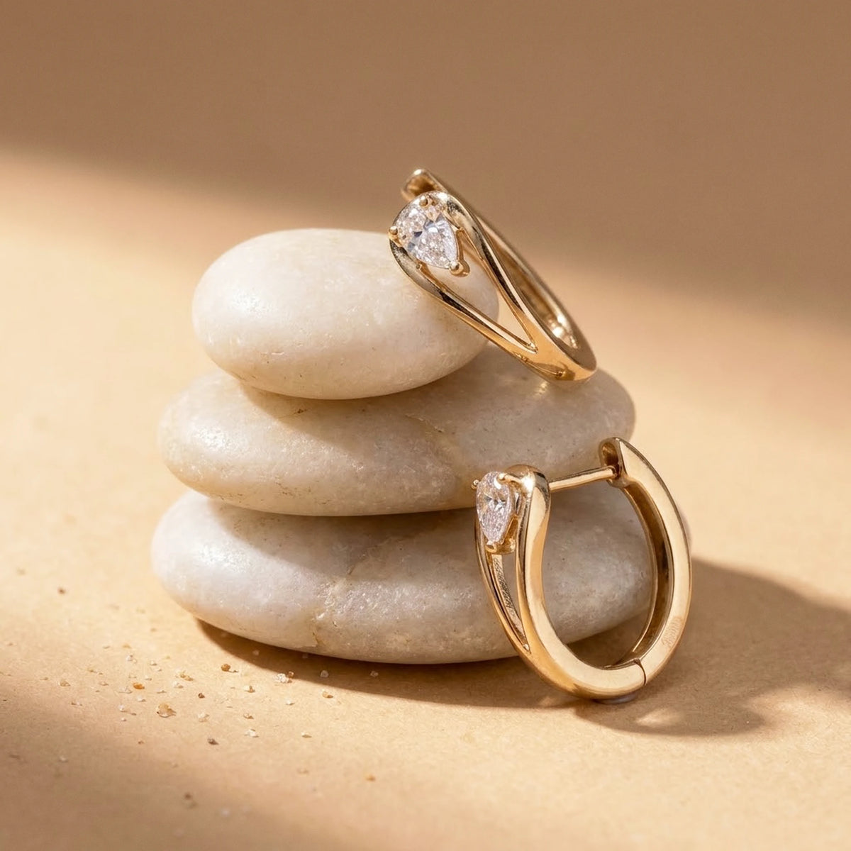 18K gold plated pear cut crystal huggie hoop earrings, still life on smooth stones | SKU: AUR-PRCZHG-G