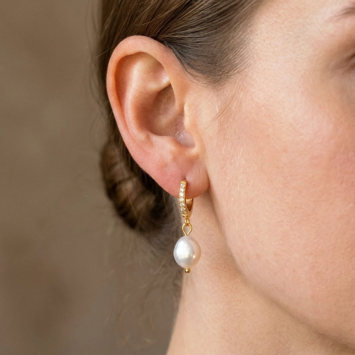 18K gold plated freshwater pearl drop huggie earrings, worn close up on the ear