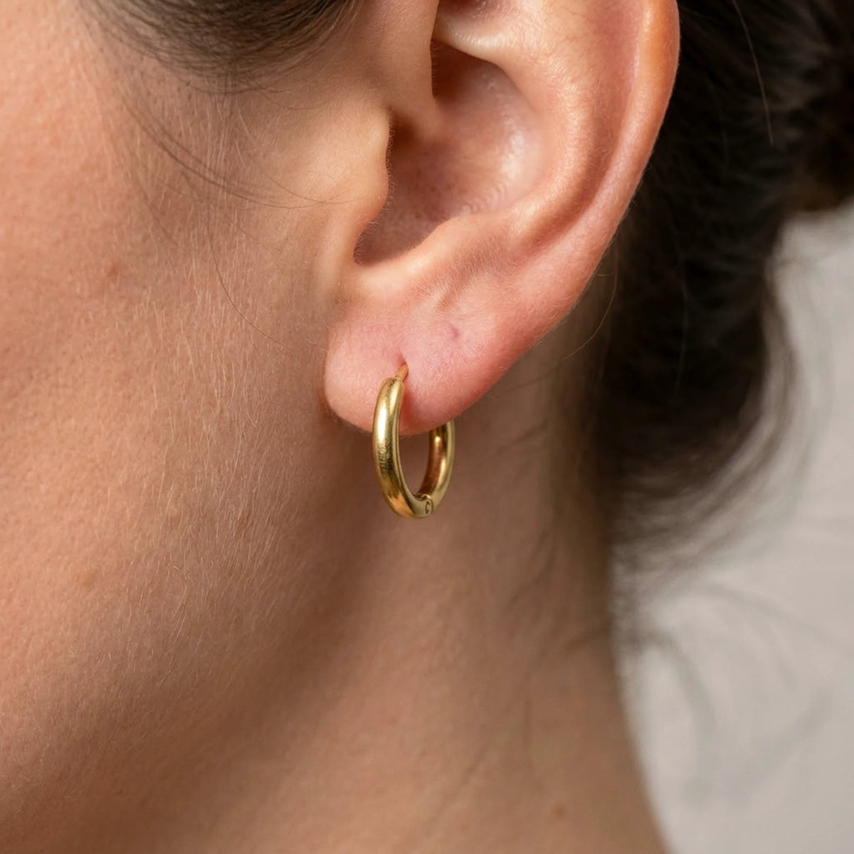 18K gold plated tiny huggie hoop earrings, macro detail on the earlobe | SKU: AUR-TNYHUG-G