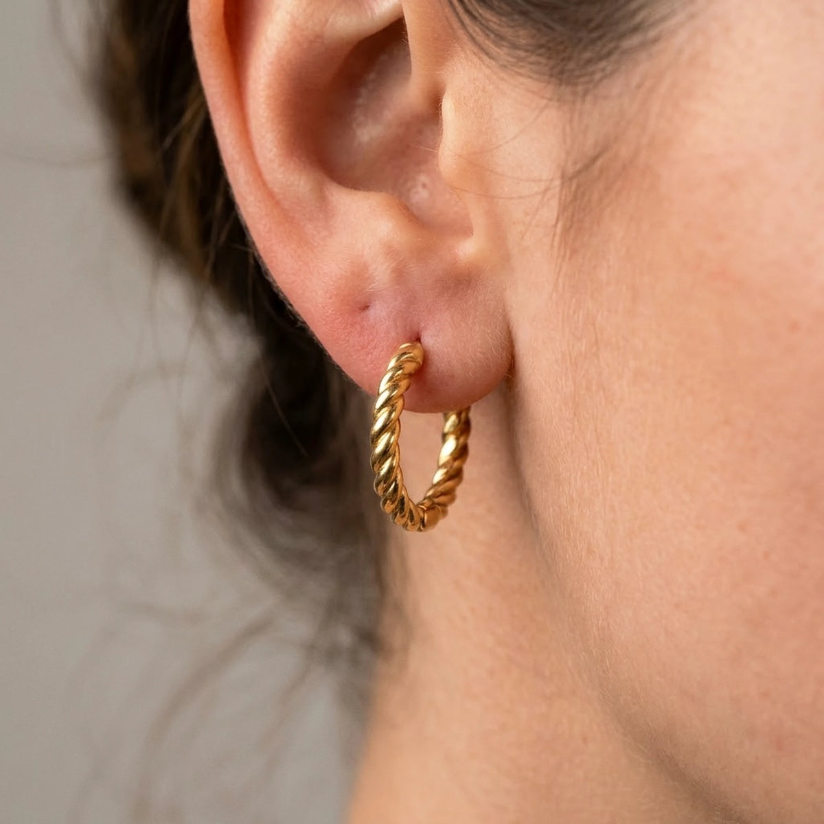 18K gold plated twisted rope huggie hoop earrings, macro detail on the earlobe | SKU: AUR-TWRHUG-G