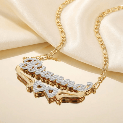 Double Heart Name Necklace with Figaro Chain by AUREATE featuring a gold and silver plated design on a satin background.