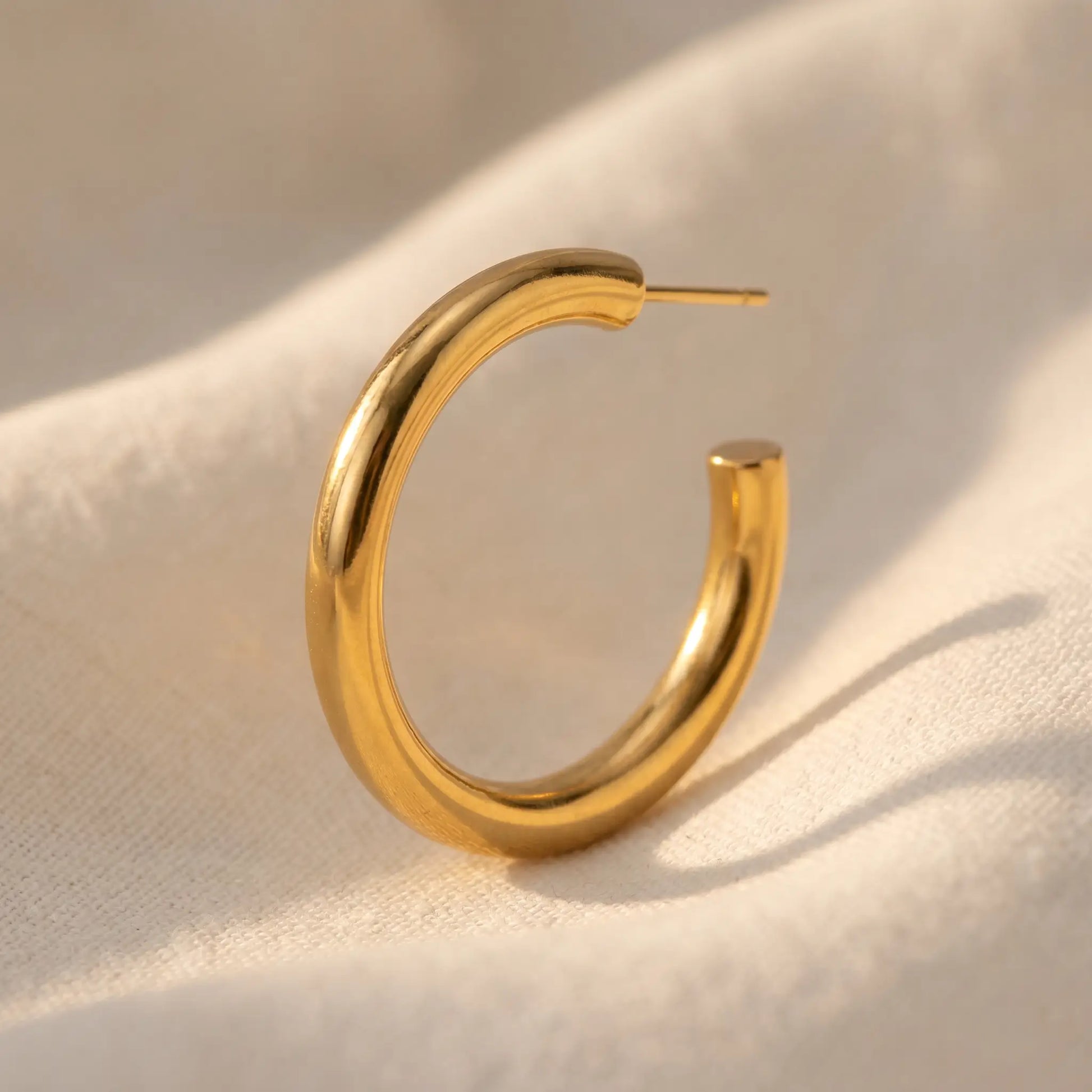 Chunky Gold Hoop Earring single - architectural close-up on cream linen