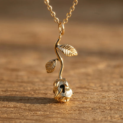 AUREATE Rose Flower Charm Pendant 18K Gold macro detail on raw oak wood — sculpted petals, engraved leaf veining and curving stem revealing craftsmanship.