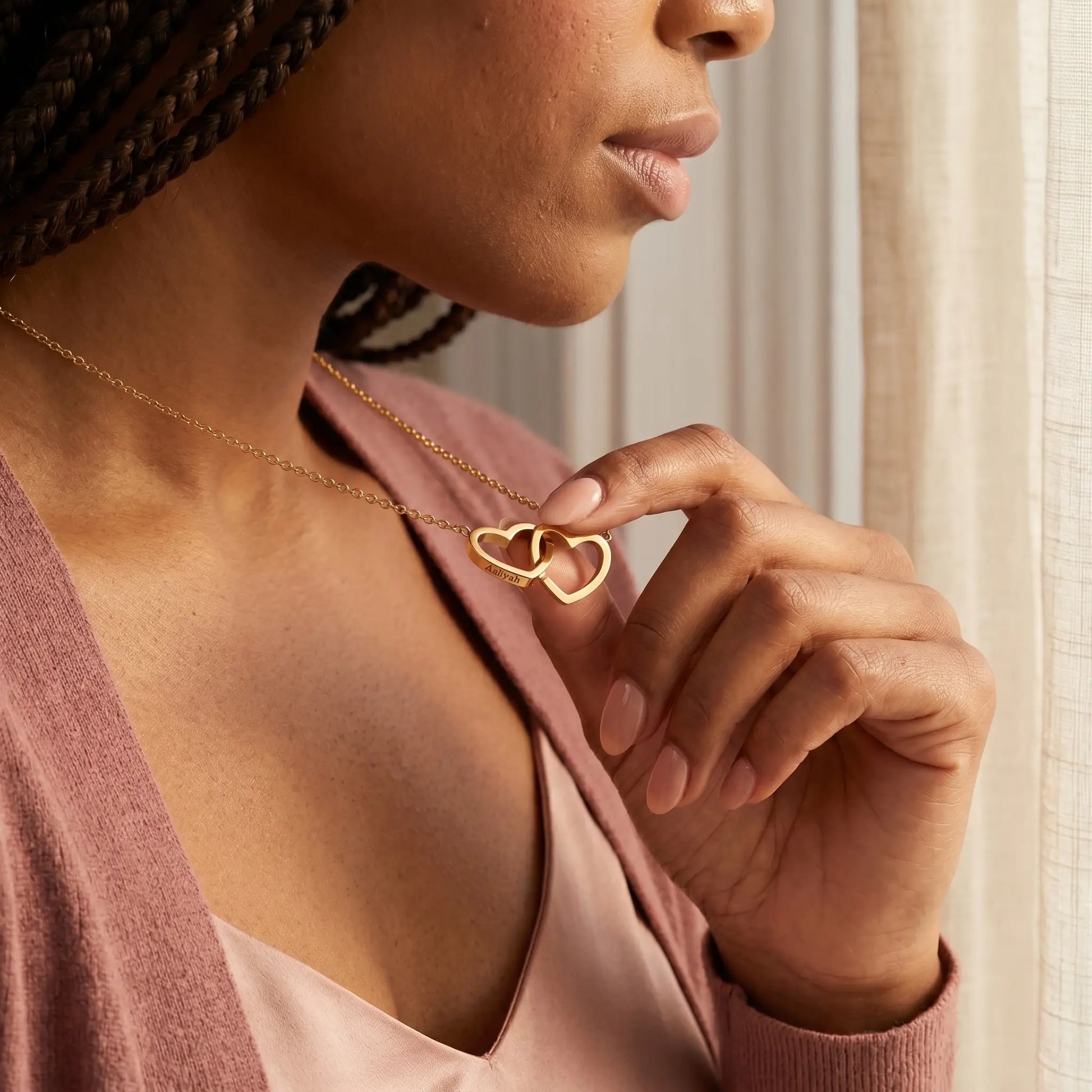 Engraved Double Heart Pendant 18K Gold lifestyle hand close-up, fingertips touching personalized Aaliyah engraving on interlocked hearts intimate daily ritual moment