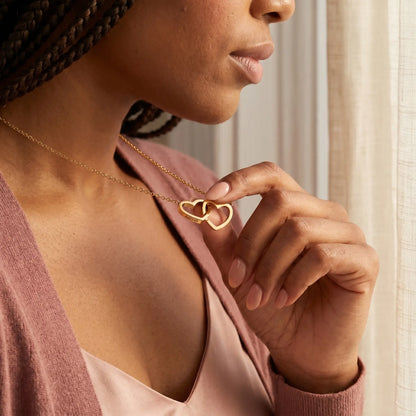 Engraved Double Heart Pendant 18K Gold lifestyle hand close-up, fingertips touching personalized Aaliyah engraving on interlocked hearts intimate daily ritual moment