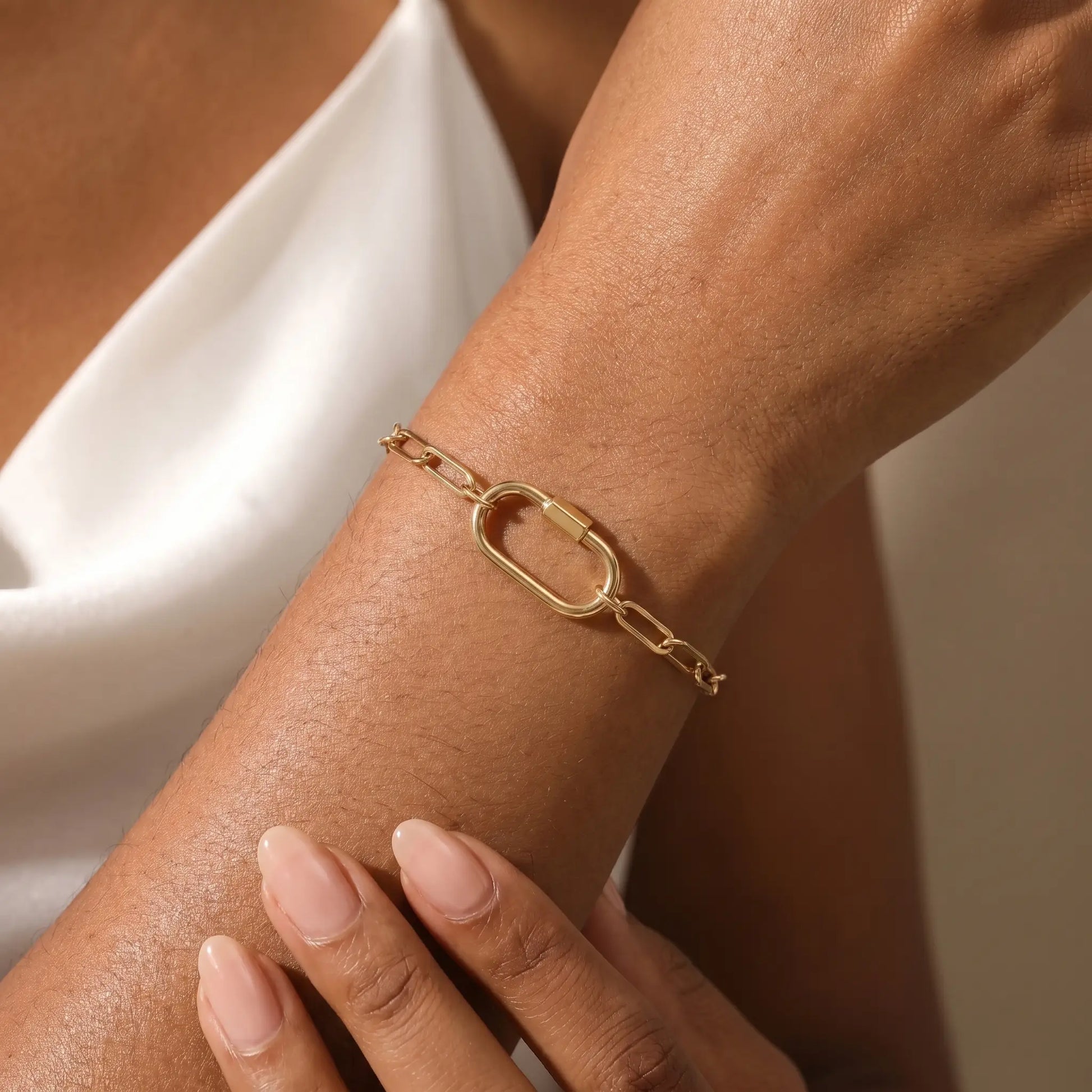 Gold paperclip bracelet with oval carabiner lock pendant worn on woman's wrist - 18K gold plated stainless steel