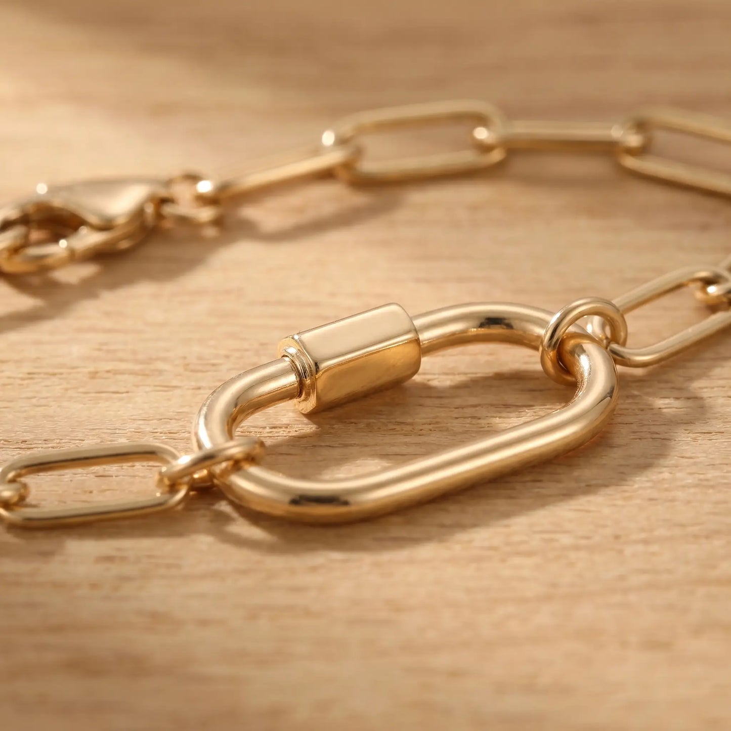 Gold paperclip bracelet macro detail of oval carabiner lock pendant