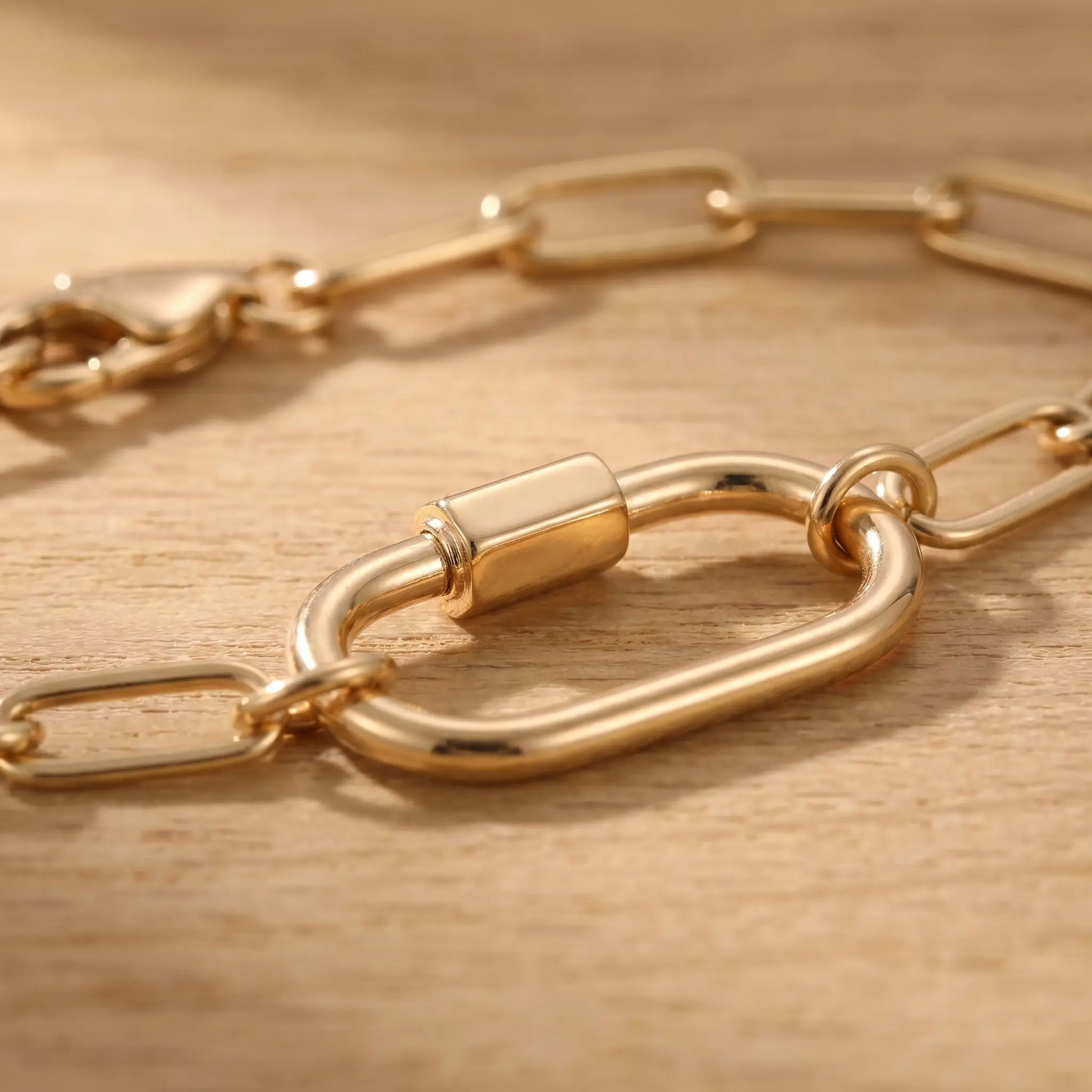 Gold paperclip bracelet macro detail of oval carabiner lock pendant