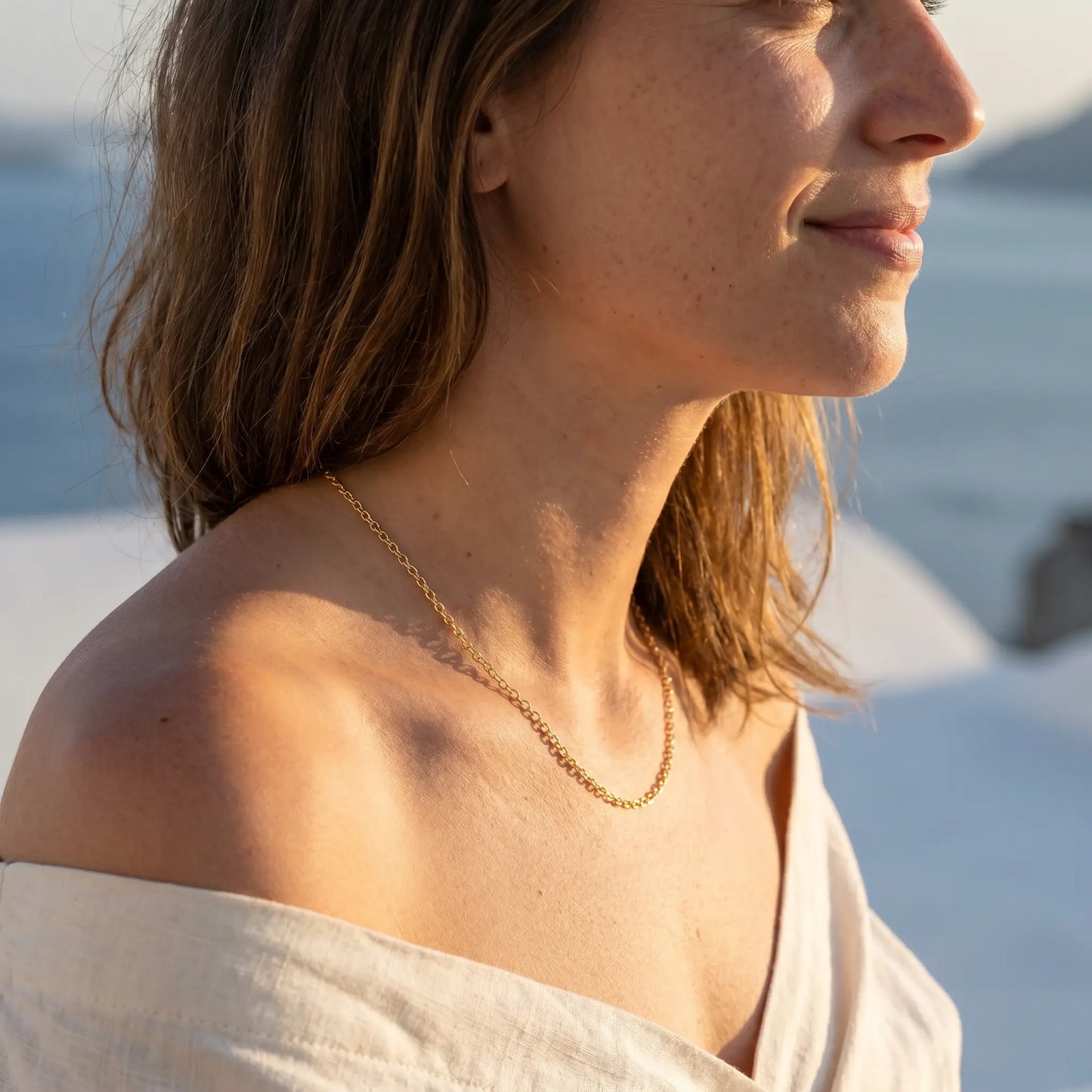 Gold collarbone necklace profile subtle smile Santorini sunset