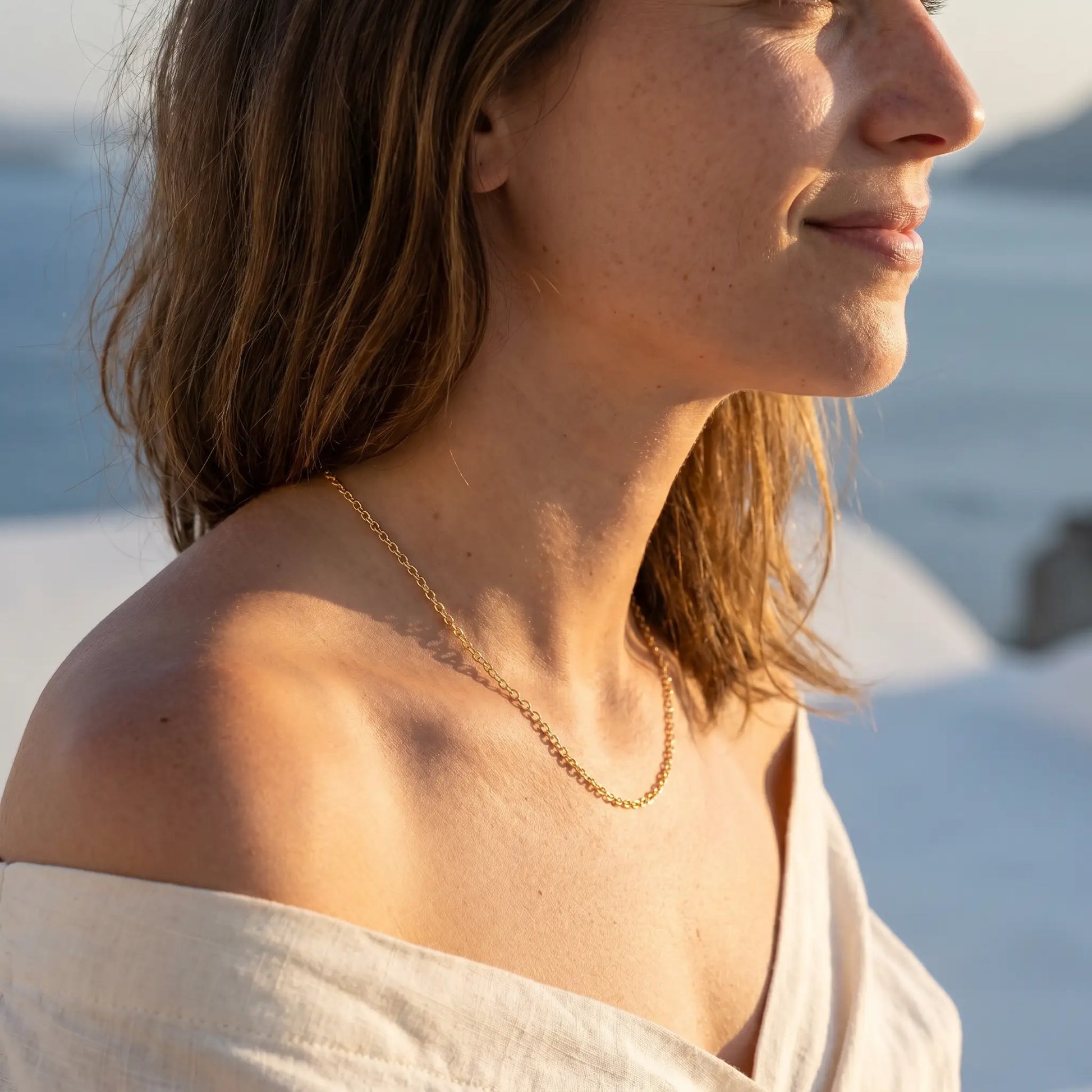 Gold collarbone necklace profile subtle smile Santorini sunset