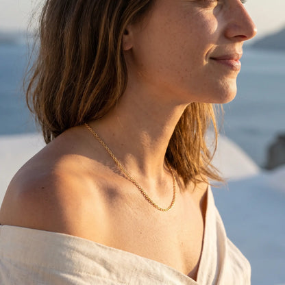 Gold collarbone necklace profile subtle smile Santorini sunset