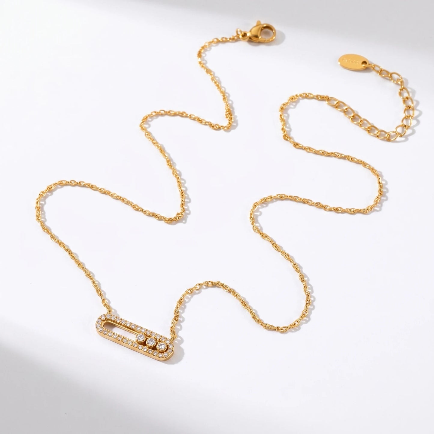 Gold paperclip pendant necklace flat lay packshot with pavé halo and 3 floating CZ stones, thin cable chain