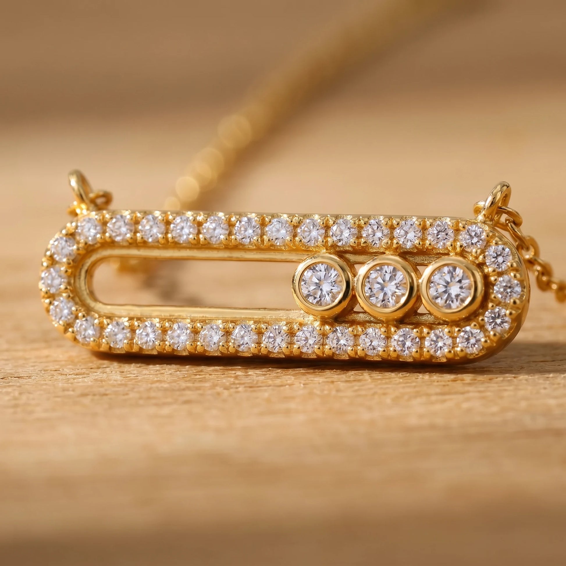 Macro detail of gold pavé halo paperclip pendant with 3 bezel-set cubic zirconia stones