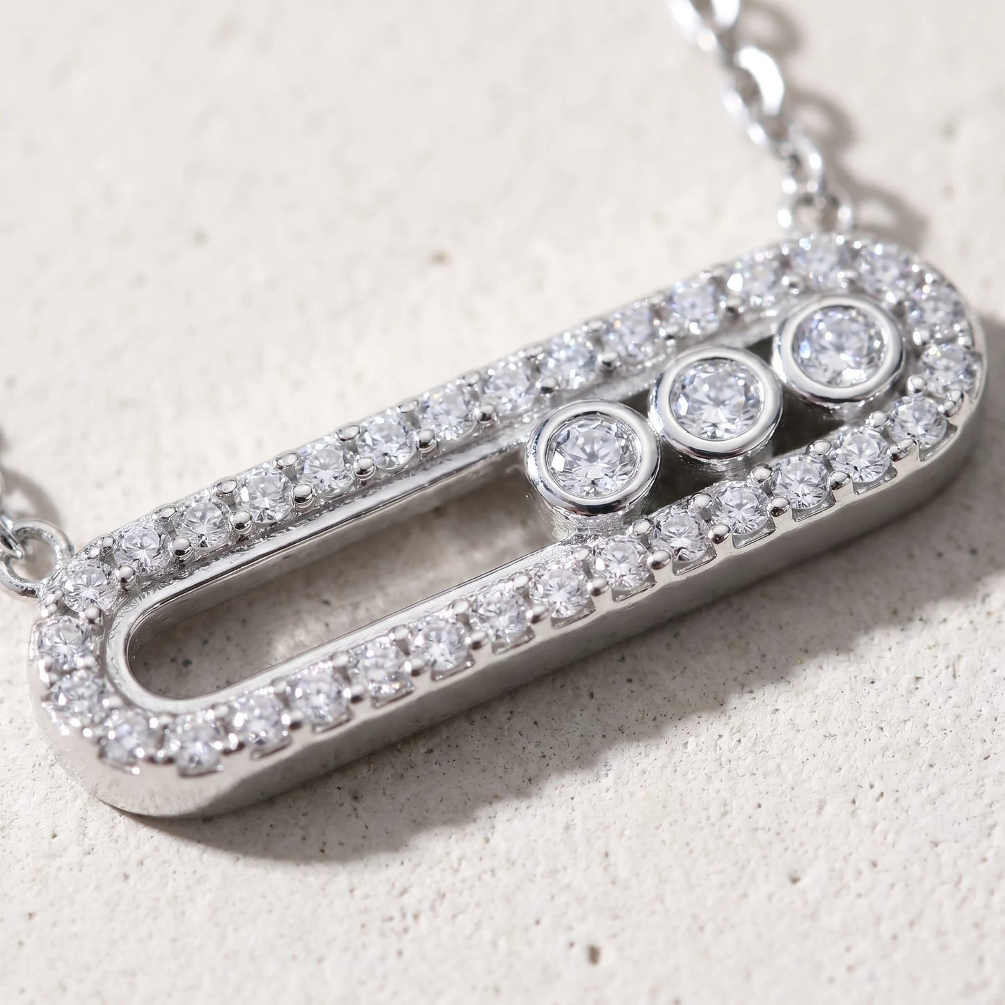 Macro detail of silver pavé halo paperclip pendant with 3 bezel-set cubic zirconia stones