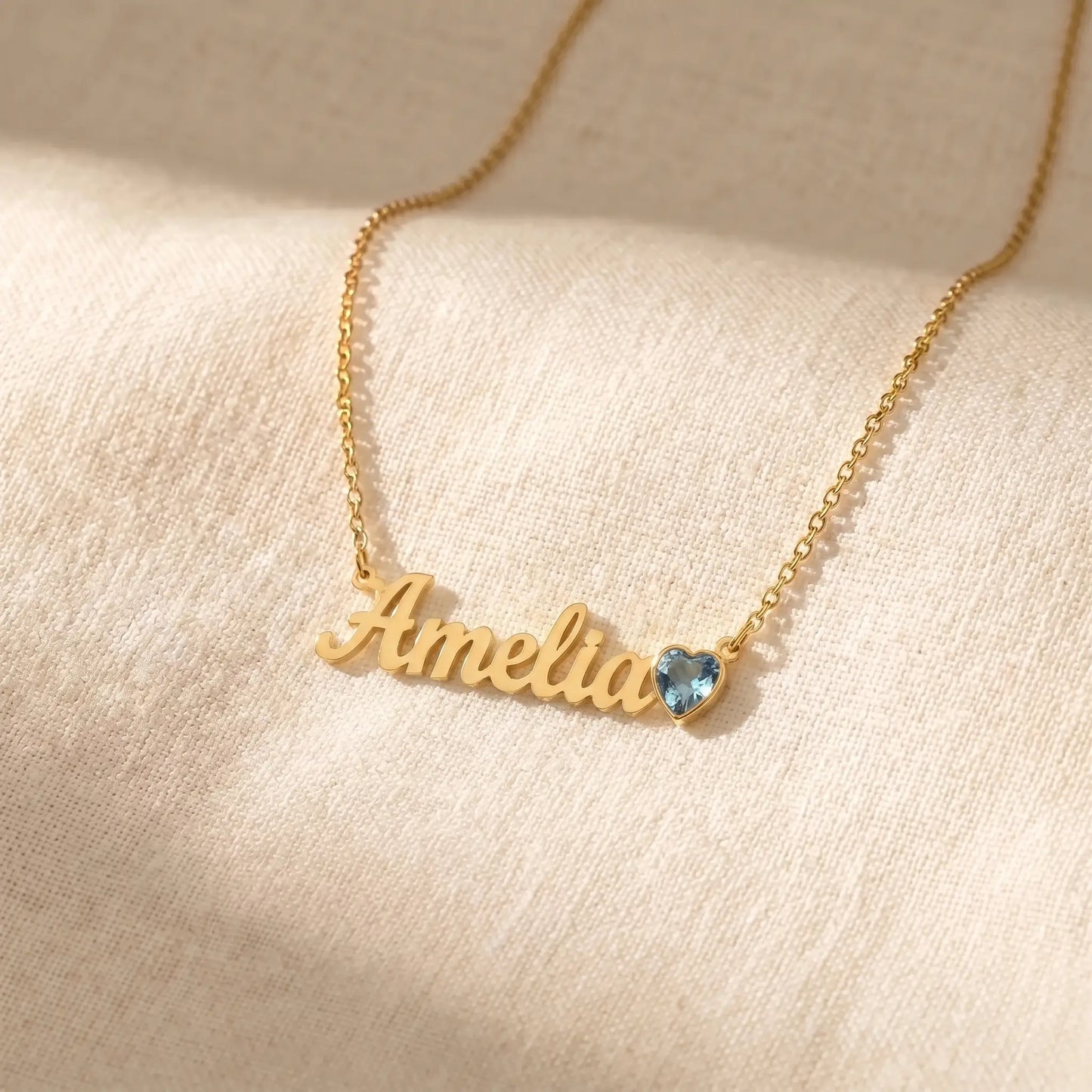 Birth Stone Letter Drop Strand 18K Gold flat-lay on cream linen with Amelia cursive name and March Aquamarine heart birthstone