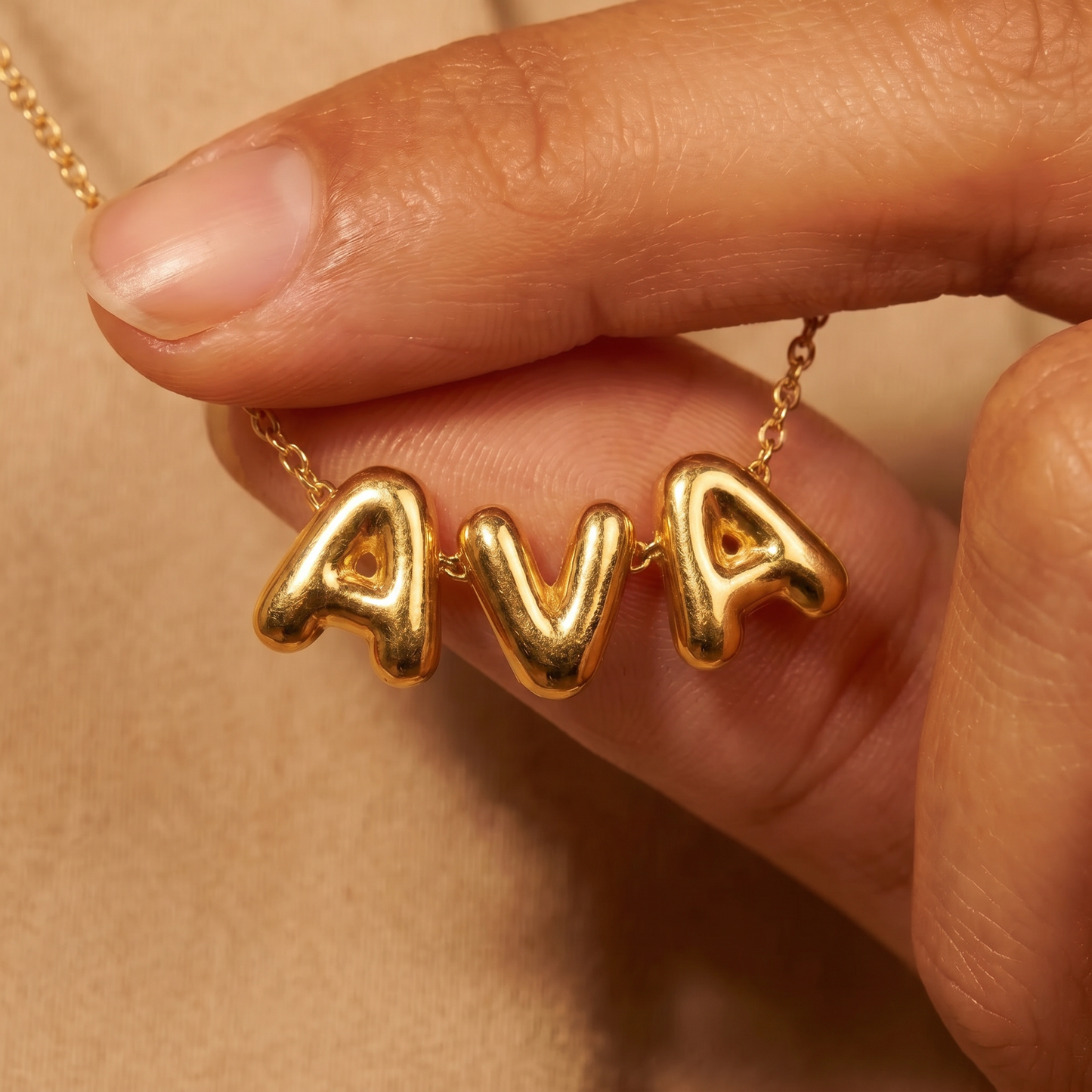 Gold puffy bubble-letter name necklace AVA held in hand, fine cable chain