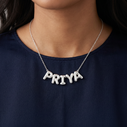 Silver puffy bubble-letter name necklace PRIYA worn on navy top, fine cable chain