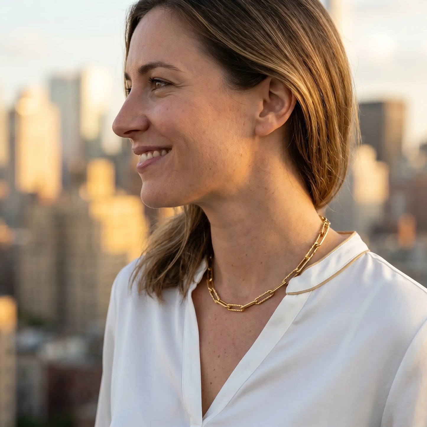 Mixed paperclip necklace gold lifestyle profile — NYC rooftop Manhattan skyline golden hour white silk blouse