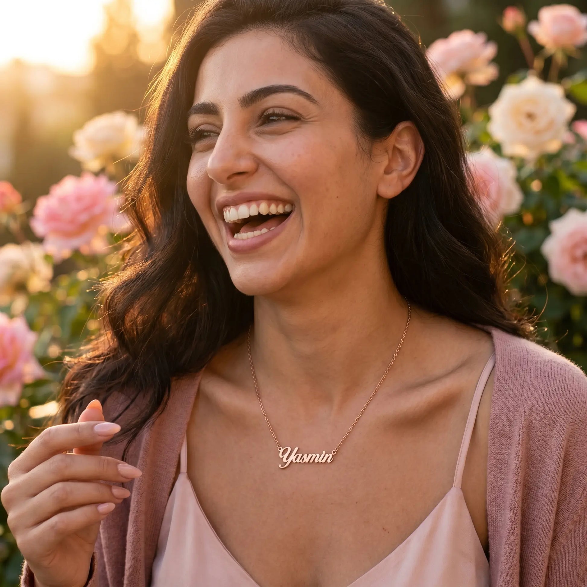 Young woman laughing outdoors, wearing a Personalised Plate Chain in 18K Gold by AUREATE, surrounded by flowers.
