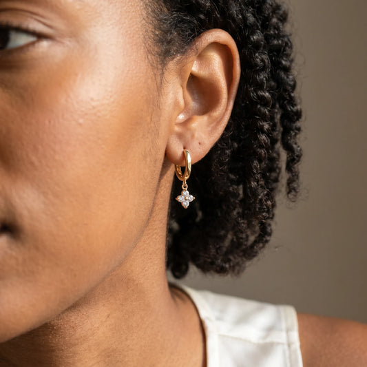 Gold petite clover huggie earrings worn close-up