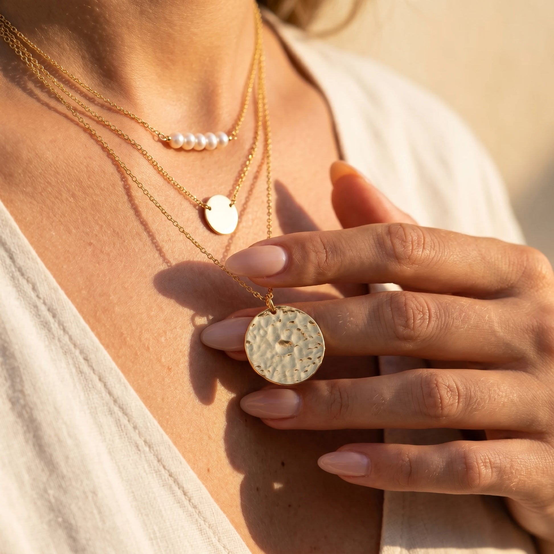 Fingertips touching large hammered gold coin pendant Riviera lifestyle