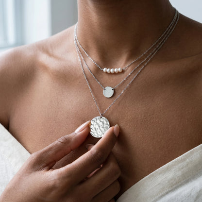 Fingertips touching large hammered silver coin pendant art gallery lifestyle