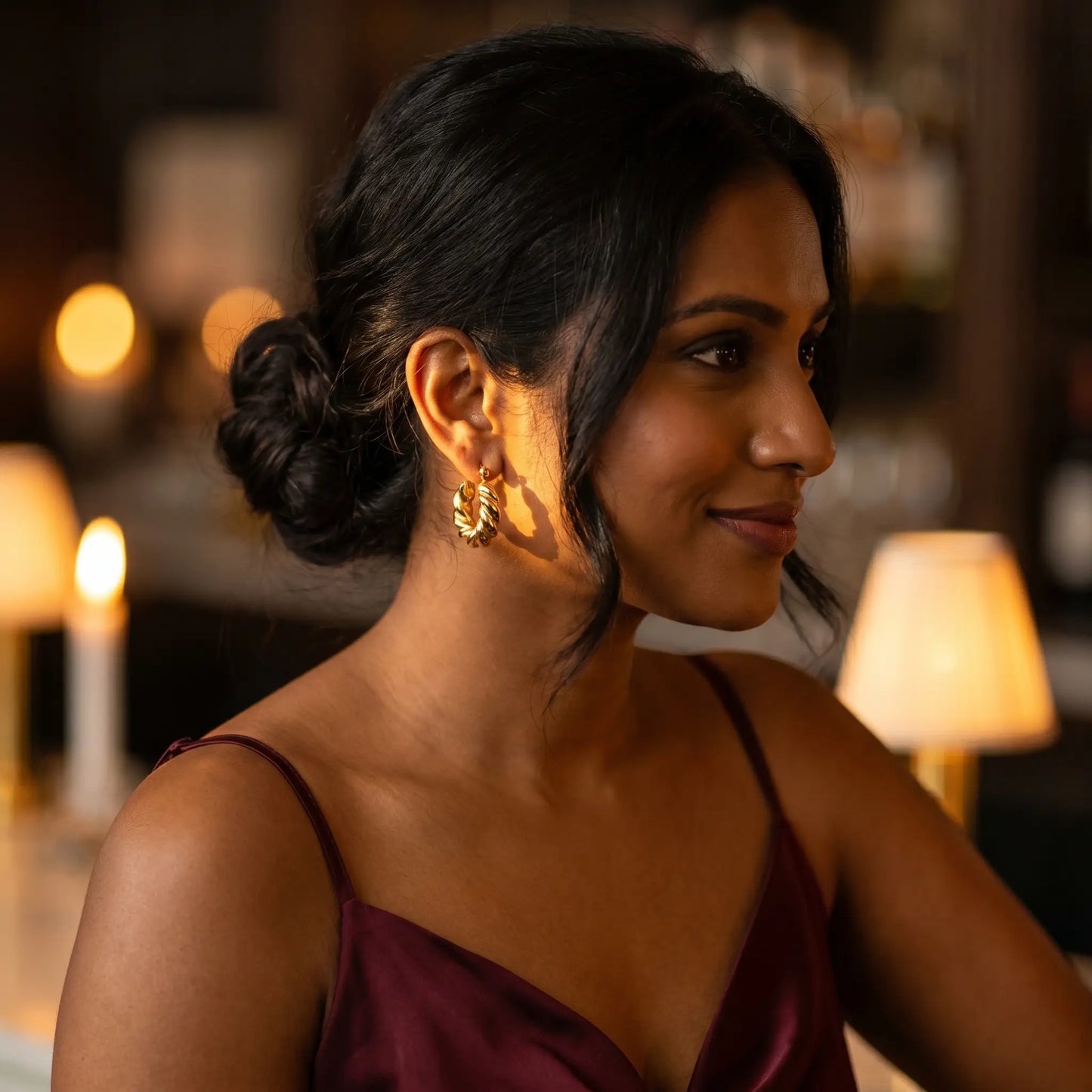 Woman at cocktail bar wearing Twisted Gold Hoop Earrings - evening candlelight