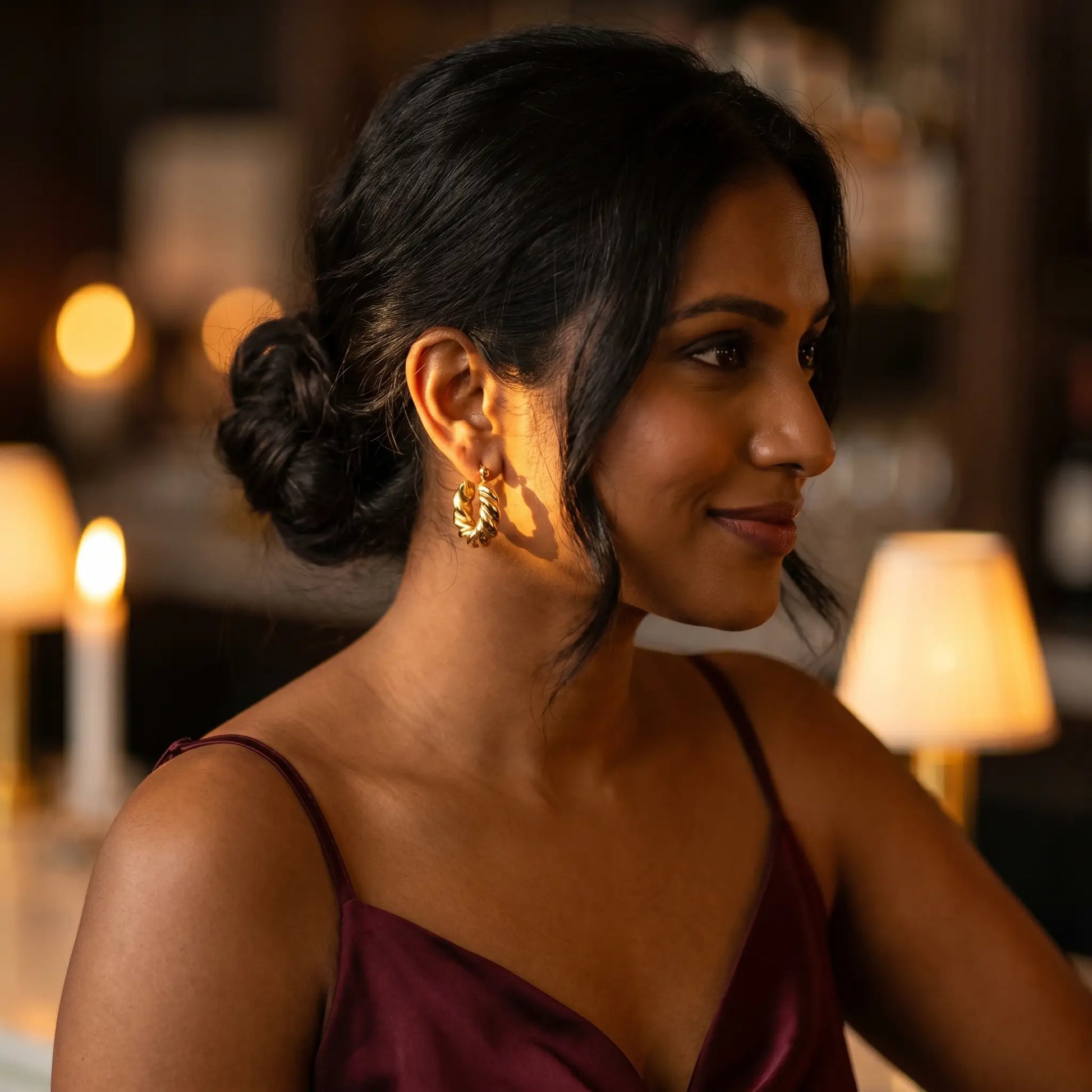 Woman at cocktail bar wearing Twisted Gold Hoop Earrings - evening candlelight