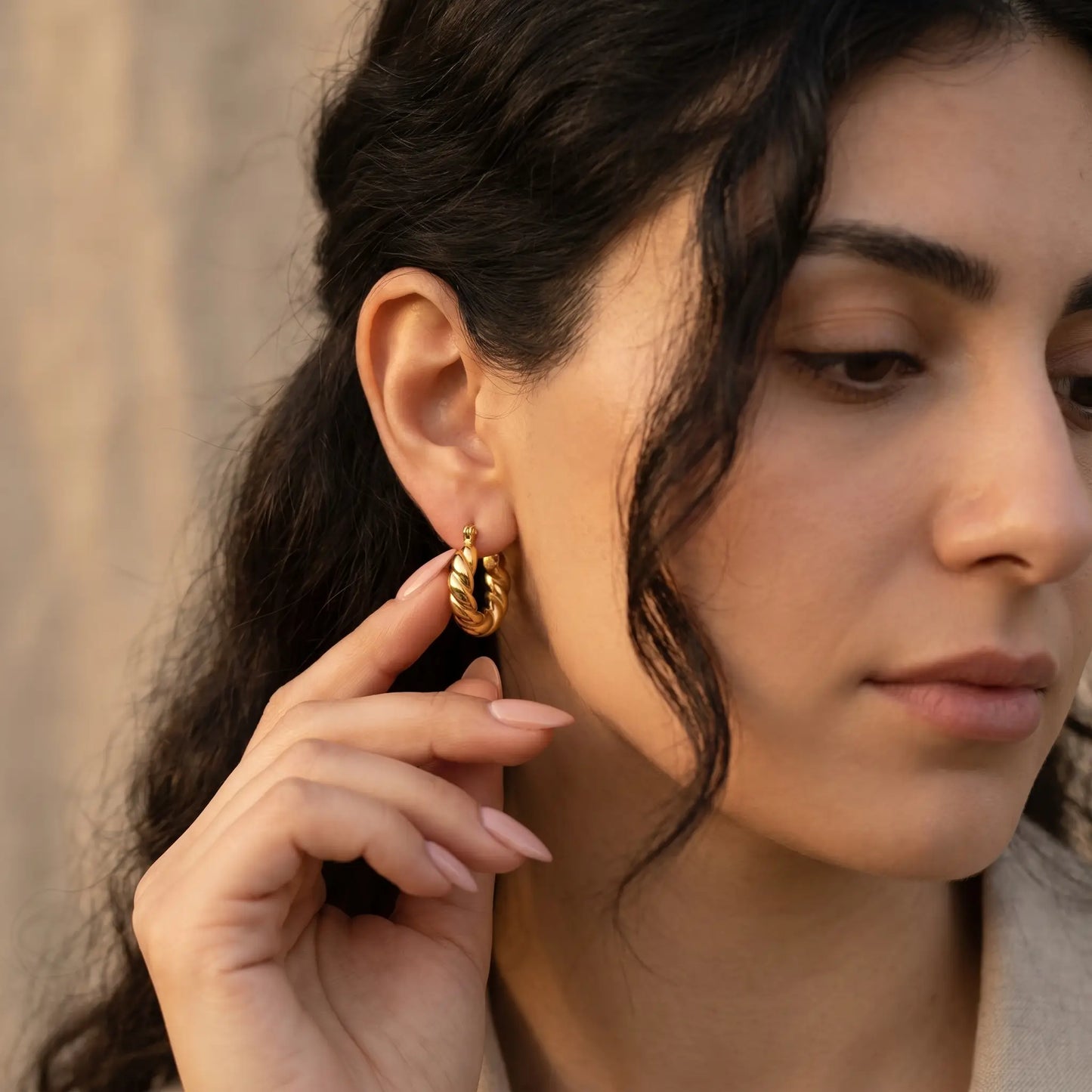 Woman touching Twisted Gold Hoop Earring - studio hand-to-ear